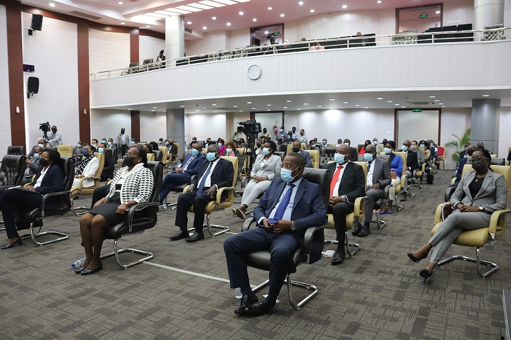 Participantes sentados num auditório durante um evento formal, a maioria usando máscara e traje profissional. O espaço é amplo, com cadeiras organizadas e uma galeria superior ao fundo.